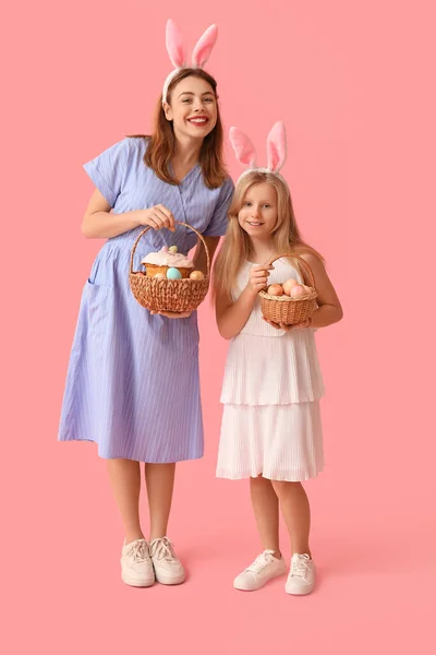 可爱的小女孩和她的母亲戴着兔子耳朵 手里拿着一篮子粉色背景彩绘鸡蛋的复活节蛋糕 — 图库照片