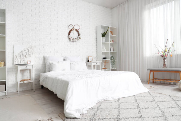 Интерьер светлой спальни с пасхальным венком, столами и полками