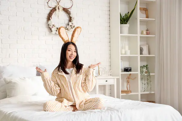 Yatak odasında oturan tavşan kulaklı genç Asyalı kadın. Paskalya kutlaması