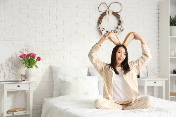 Yatak odasında oturan tavşan kulaklı genç Asyalı kadın. Paskalya kutlaması