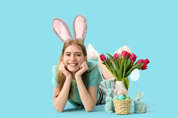 Молода Жінка Кролячих Вухах Великодніми Кроликами Яйцями Тюльпанами Лежить Синьому — стокове фото