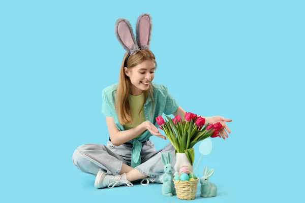Молода Жінка Кролячих Вухах Великодніми Кроликами Яйцями Тюльпанами Сидить Синьому — стокове фото