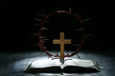 Ahşap haçlı dikenli taç, siyah grunge arka planda İncil ve ışık