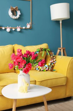 Vase with tulips and Easter rabbit on table in living room