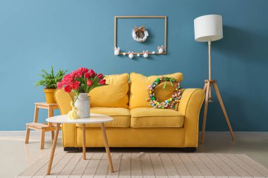 Paskalya çelenkleri, kanepesi ve masası olan bir oturma odası.