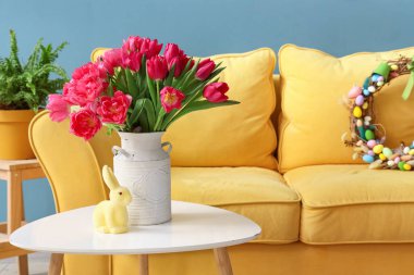 Vase with tulips and Easter rabbit on table in living room
