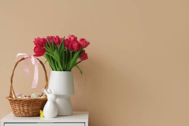 İçinde lale ve Paskalya yumurtası olan vazo bej duvarın yanında.