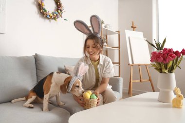 Paskalya yumurtası ve evde tavşan kulaklı sevimli bir av köpeği olan genç bir kadın.