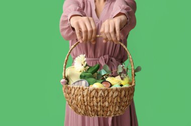 Yeşil arka planda kozmetik ürünleri olan hasır Paskalya sepeti tutan genç bir kadın.