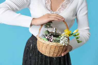 Mavi arka planda kozmetik ürünleri olan hasır Paskalya sepeti tutan genç bir kadın.