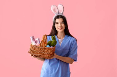 Pembe arka planda Paskalya yumurtaları olan tavşan kulaklı kadın doktor.