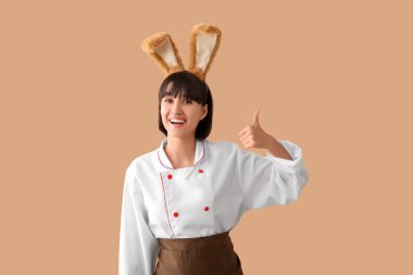 Tavşan kulaklı kadın aşçı kahverengi arka planda baş parmağını kaldırıyor. Paskalya kutlaması