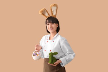 Tavşan kulaklı kadın aşçı Paskalya tavşanı ve kahverengi arka planda yumurtalar.