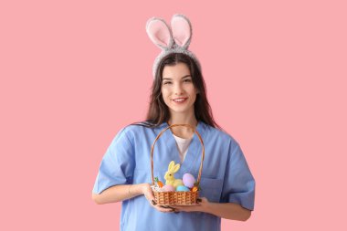 Pembe arka planda Paskalya yumurtaları olan tavşan kulaklı kadın doktor.