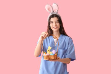 Pembe arka planda Paskalya yumurtaları olan tavşan kulaklı kadın doktor.
