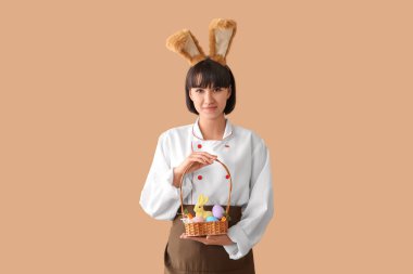 Kahverengi arka planda Paskalya yumurtaları olan tavşan kulaklı kadın aşçı.