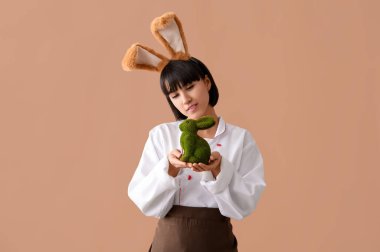 Kahverengi arka planda Paskalya tavşanı olan tavşan kulaklı kadın şef.