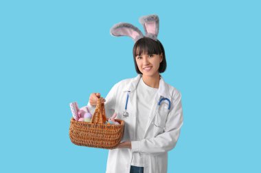 Mavi arka planda Paskalya yumurtaları olan tavşan kulaklı kadın doktor.