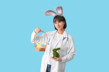 Paskalya tavşanı ve mavi arka planda yumurtaları olan tavşan kulaklı kadın doktor.