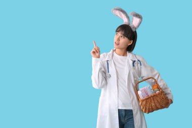 Tavşan kulaklı kadın doktor. Paskalya yumurtaları mavi arka plandaki bir şeyi işaret ediyor.