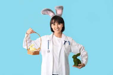 Paskalya tavşanı ve mavi arka planda yumurtaları olan tavşan kulaklı kadın doktor.