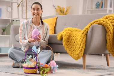 Paskalya yumurtasıyla evde oturan genç bir kadın.