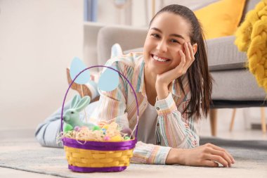 Paskalya yumurtası dolu sepeti olan genç bir kadın evde yerde yatıyor.