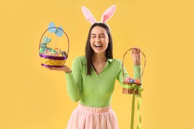 Tavşan kulaklı, sarı arka planda Paskalya yumurtası sepetleri olan genç bir kadın.
