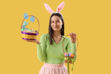 Tavşan kulaklı, sarı arka planda Paskalya yumurtası sepetleri olan genç bir kadın.