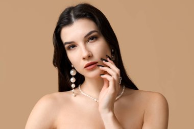 Kahverengi arka planda zarif inci mücevherleri olan güzel genç bir kadın.