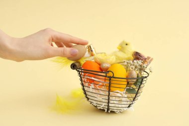 Sepet dolusu parfüm, Paskalya yumurtası ve sarı arka planda bebek tavuğu olan bir kadın eli.