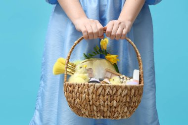 Mavi arka planda dekoratif kozmetik dolu sepeti olan güzel genç bir kadın.