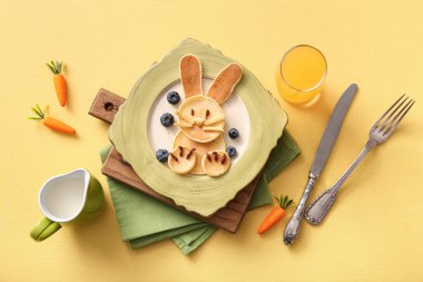 Sarı arka planda bir bardak portakal suyu olan komik Paskalya tavşanı krepleri.