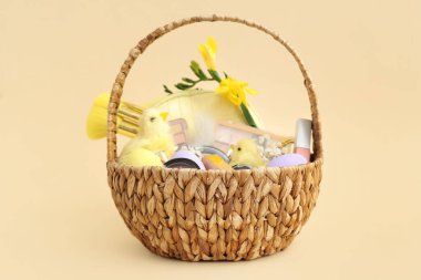 Dekoratif kozmetik ürünleri, bebek tavuklar ve bej arka planda Paskalya yumurtaları olan hasır sepet.