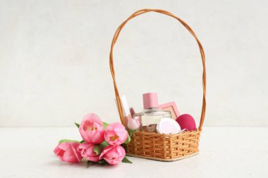 Dekoratif kozmetik ürünleriyle hasır Paskalya sepeti ve beyaz arka planda bir buket lale.