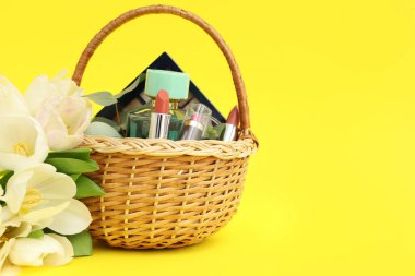Hasır Paskalya sepeti, dekoratif kozmetik ürünleri ve sarı arka planda çiçekler.