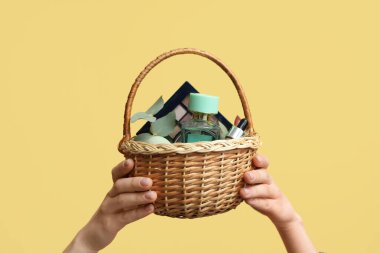 Hasır paskalya sepeti dekoratif kozmetik ve sarı arka planda okaliptüs dolu kadın elleri.