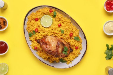 Sarı arka planda malzemelerle geleneksel tavuk biryani tabağı.
