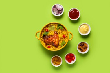 Bir kase geleneksel tavuk biryani ve yeşil arka planda malzemeler.