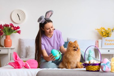 Paskalya yumurtası ve yatak odasında Pomeranya köpeği olan genç bir kadın.