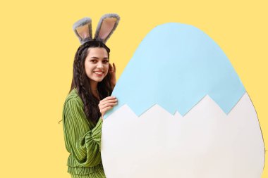 Tavşan kulaklı güzel bir kadın. Sarı arka planda büyük bir paskalya yumurtası.