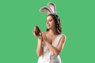 Yeşil arka planda çikolatalı Paskalya yumurtası olan tavşan kulaklı güzel bir kadın.