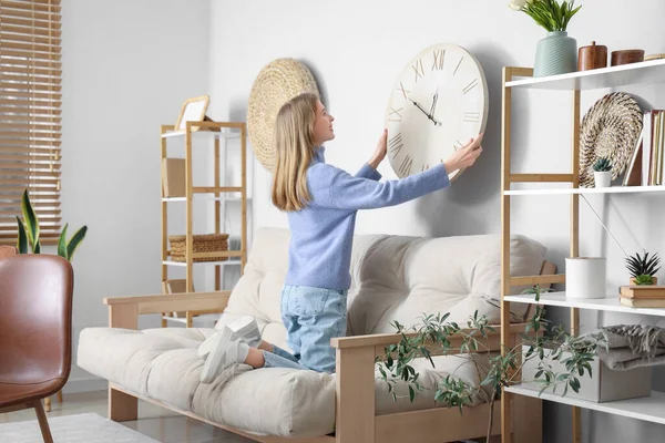 Young woman hanging big clock on wall at home