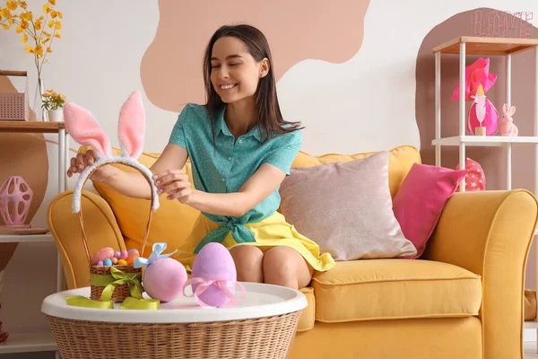 Tavşan kulaklı ve Paskalya yumurtası sepeti evde oturan genç bir kadın.