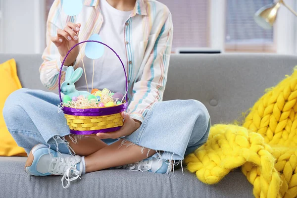 Paskalya yumurtası sepeti olan genç bir kadın evdeki kanepede oturuyor, yakın plan.