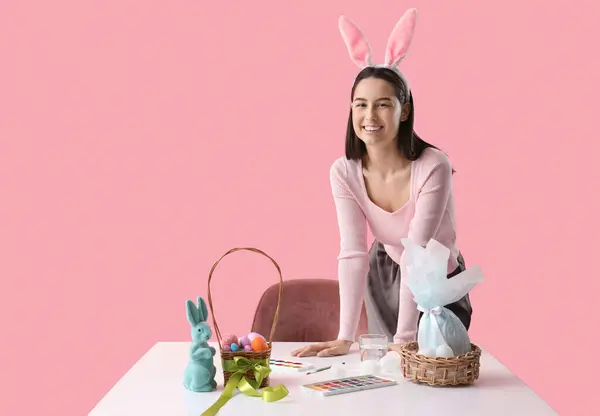 Fiatal Nyuszifül Kosár Húsvéti Tojás Festékek Asztalnál Rózsaszín Háttér — Stock Fotó