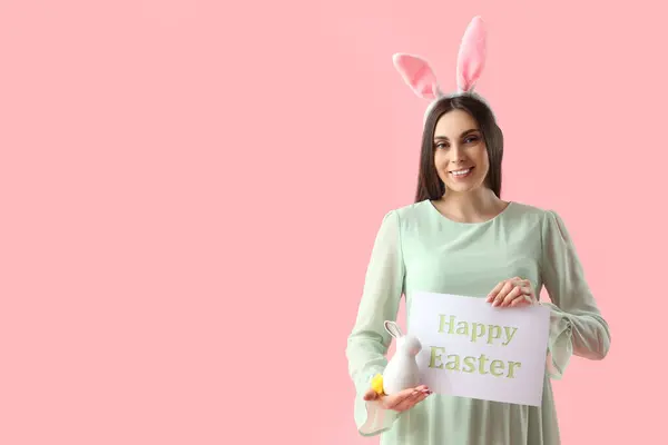 带复活节兔子和粉色背景卡片的兔子耳朵中的年轻孕妇 — 图库照片