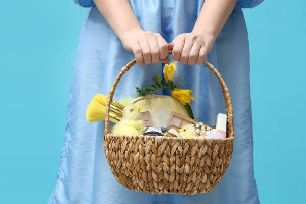 Mavi arka planda dekoratif kozmetik dolu sepeti olan güzel genç bir kadın.