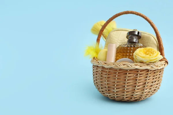 Wicker Easter basket with decorative cosmetics and flowers on blue background