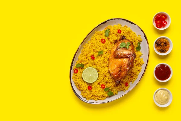 Sarı arka planda farklı baharatlarla geleneksel tavuk biryani tabağı.